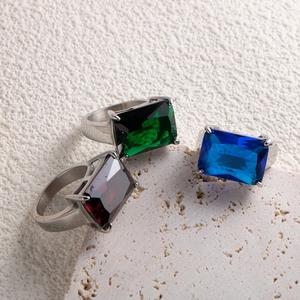Three queen rings with large rectangle green, blue, and red gems on beige stone