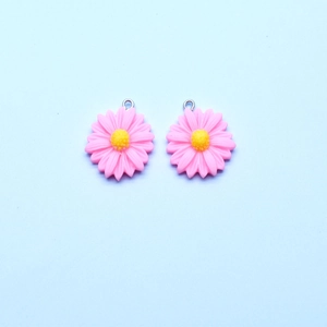 Macro shot of two pink resin daisy pendants with yellow centers and metal rings for DIY