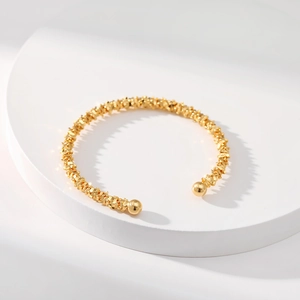Elegante brazalete dorado con textura irregular y extremos de bolas redondas