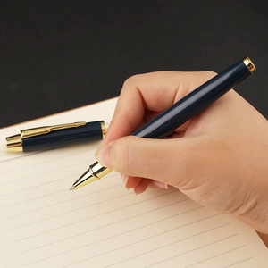 Classic navy blue metal rollerball pen with gold trim writing on a notebook