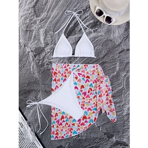 Detailed flat lay of a white three-piece bikini set with a colorful heart print sarong