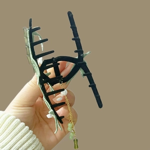 Close-up of black matte hair claw with green embroidery, gold chain tassel and pearl bead