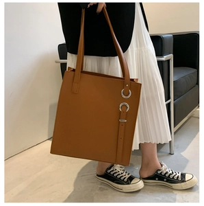 Close-up of a large brown leather tote bag with silver ring detail and long strap
