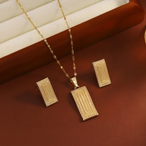 Detail of golden jewelry set showing geometric texture on necklace pendant and earrings