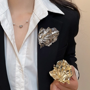 Macro detail of abstract pleated leaf brooches in gold and silver on a black blazer