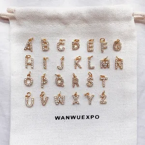 Detailed view of 26 golden alphabet pendants with clear crystals on white linen fabric