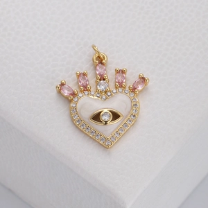 Macro view of gold heart crown charm with white enamel evil eye and pink gemstones