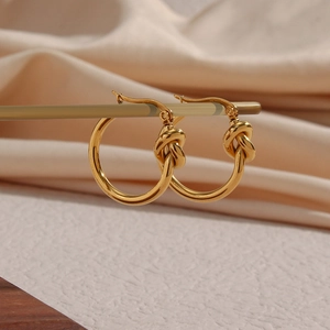 Minimalist gold titanium steel knotted hoop earrings for women on a jewelry display stand