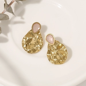 Gold hammered earrings with pink teardrop gemstones on a minimalist ceramic tray