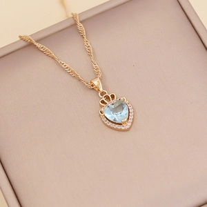 Golden heart necklace with light blue crystal and crown detail on a jewelry box