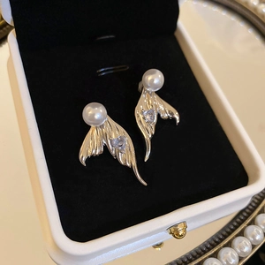 Macro view of gold mermaid tail earrings with heart zircon and white pearl in jewelry box