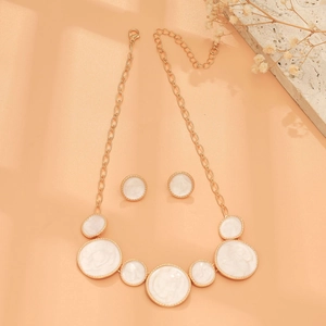 Detail view of gold necklace and earrings with round white enamel inlay on warm background
