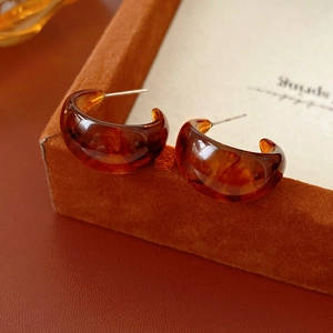 Macro view of C-shaped amber tortoiseshell resin earrings with metallic posts