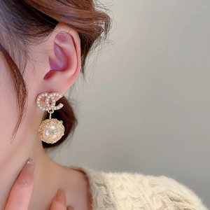 Detail view of gold earrings featuring double C design and hollow pearl sphere pendant