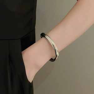 Close-up of minimalist polished silver thick round bangle worn on wrist with black outfit