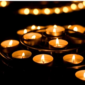 Macro view of white tea light candles on a black metal tray with warm bokeh lighting