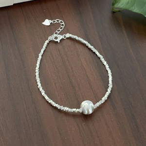 Detail of silver chain bracelet with white bead and heart charm on dark wood