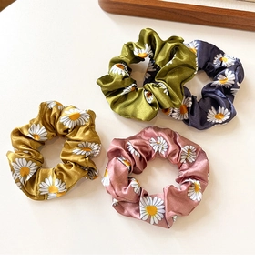 Detail of four colorful daisy print satin scrunchies with smooth silky texture