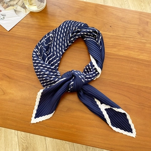 Close-up of pleated navy blue and white striped silk scarf with wavy edge on wood table