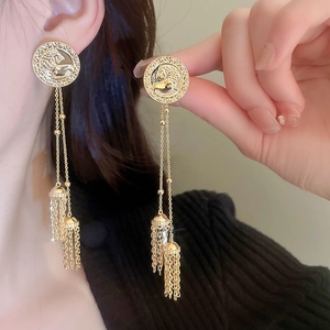 Close-up of vintage gold coin stud earrings with long metal chain tassels worn by model