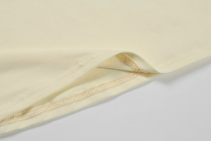 Detailed close-up of double-stitched hem and soft knit texture on a cream yellow dress