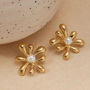Elegant gold flower stud earrings with white pearl center on a minimalist warm background