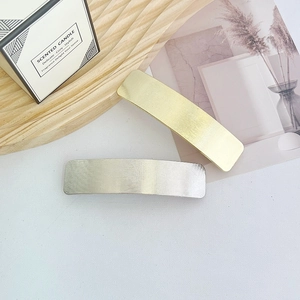 Detail of gold and silver rectangular metal hair clips with brushed texture finish
