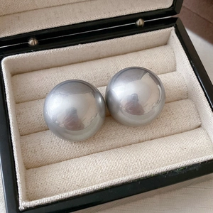 Macro detail of glossy silver spherical drop earrings displayed on a soft beige jewelry tray