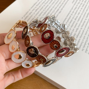 Detail of colorful enamel segments on flexible metal bracelets held by a model