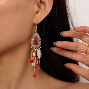 Détail de boucles d'oreilles bohèmes à pompons rouges portées sur un modèle doré