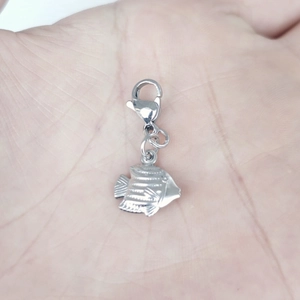 Close-up of a silver stainless steel fish pendant with lobster clasp held in a palm