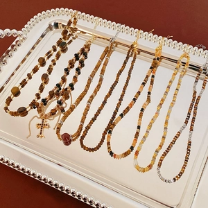 Close-up of tiger eye beaded necklaces and ornate cross pendant in a silver tray