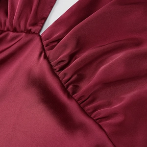 Detail of burgundy satin dress showing V-neckline with pleated fabric texture