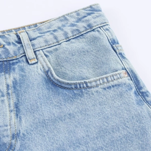 Close-up of light blue denim fabric with intricate lace stitching and high-waist belt loops