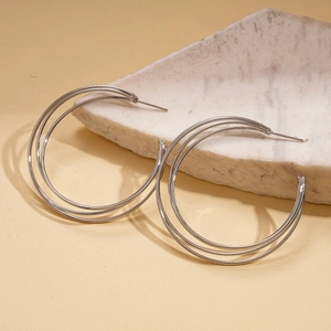 Close-up of triple-layered silver geometric C-shape hoop earrings on marble