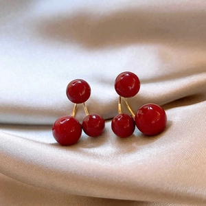 Macro shot of red berry drop earrings with gold stem on soft champagne silk fabric