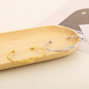 Détail de bracelets ouverts noués en finitions or et argent sur plateau bois