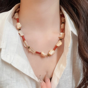 Detail of ethnic beaded necklace with shell, red resin, and tiger eye stones on model