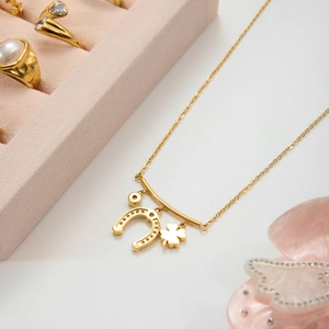 Gold stainless steel lucky necklace with four-leaf clover and horseshoe charms on jewelry box