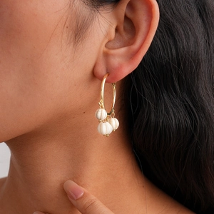 Detail of gold hoop earrings with textured white pumpkin beads worn by a model
