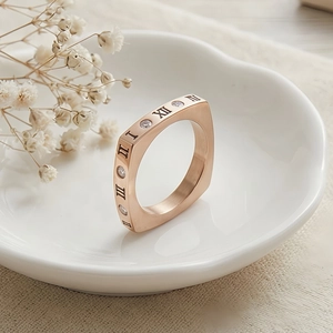 Dettaglio di un anello quadrato in oro rosa con numeri romani e zirconi scintillanti