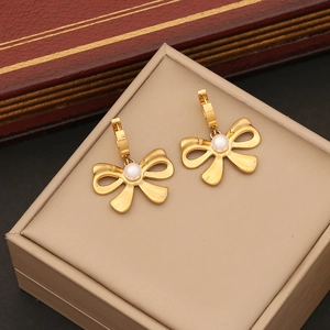 Detailed close-up of golden bow earrings with white pearls on a beige jewelry box
