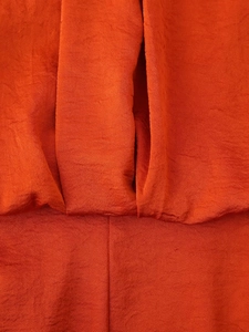 Detail shot of pleated orange satin fabric texture and stitching on the long dress