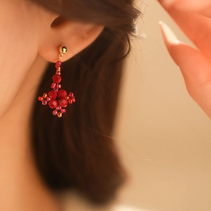 Close-up of handmade red beaded cross earrings with gold accents on model ear