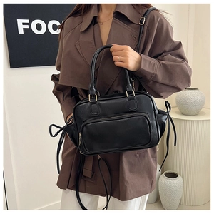 Detail of black leather handbag with decorative side bow strings on a brown trench coat