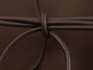 Dettaglio della cintura in pelle marrone scuro annodata sulla trama di un cardigan