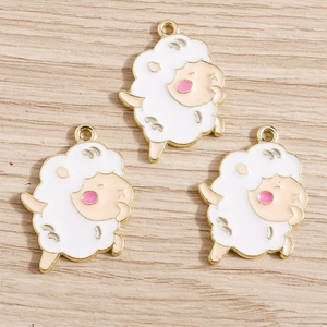 Close-up of three white and beige enamel sheep charms with gold plating on wood background