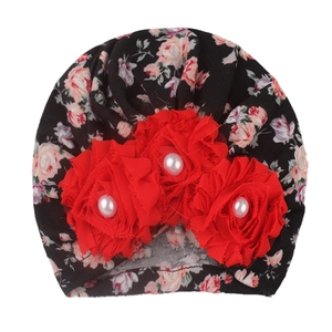 Close-up of floral baby turban hat with red fabric flowers and central pearl accents