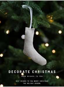 Close-up of beige knitted Christmas stocking with white pom-pom and ribbon hanging on tree