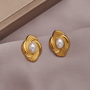 Close-up of golden swirl earrings with oval pearls resting on soft beige fabric